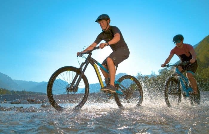 2 guys riding e-bikes through water 